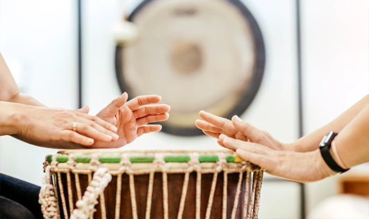 Darstellung der Musiktherapie mit einer Trommel, die von zwei Personen geschlagen wird.