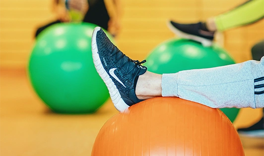 Es wird eine Gymnastikübung dargestellt, bei der ein Rehabilitand sein Unterbein auf einen Ball ablegt.